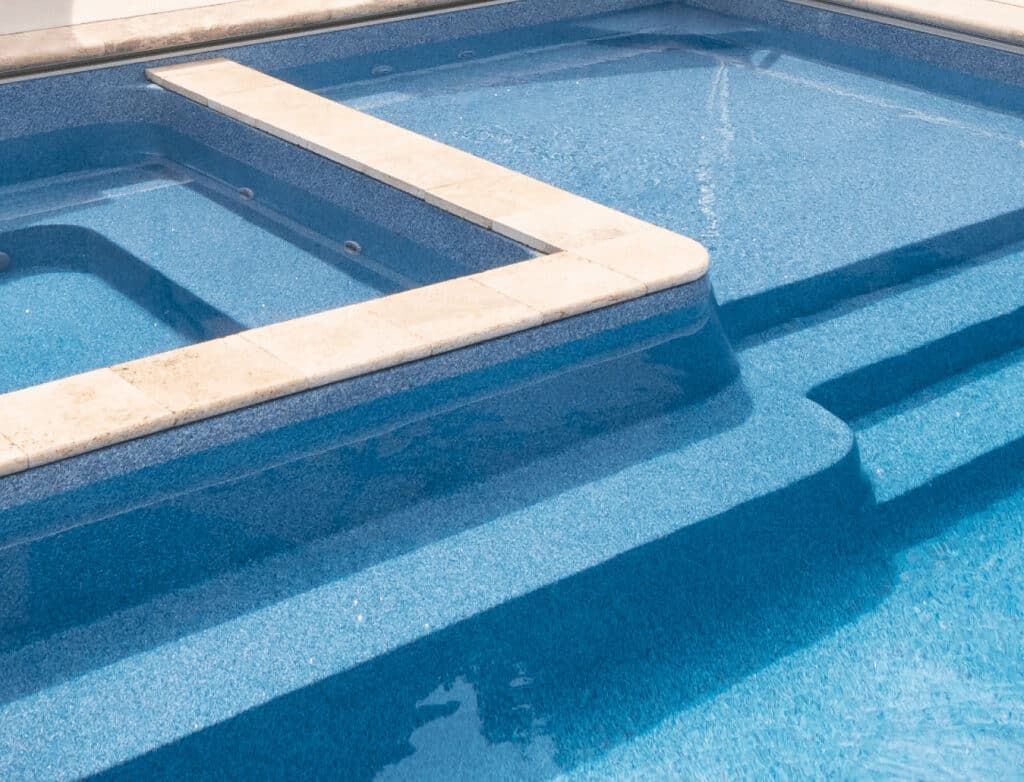 Blue tiled swimming pool with raised concrete steps and ledge in bright sunlight