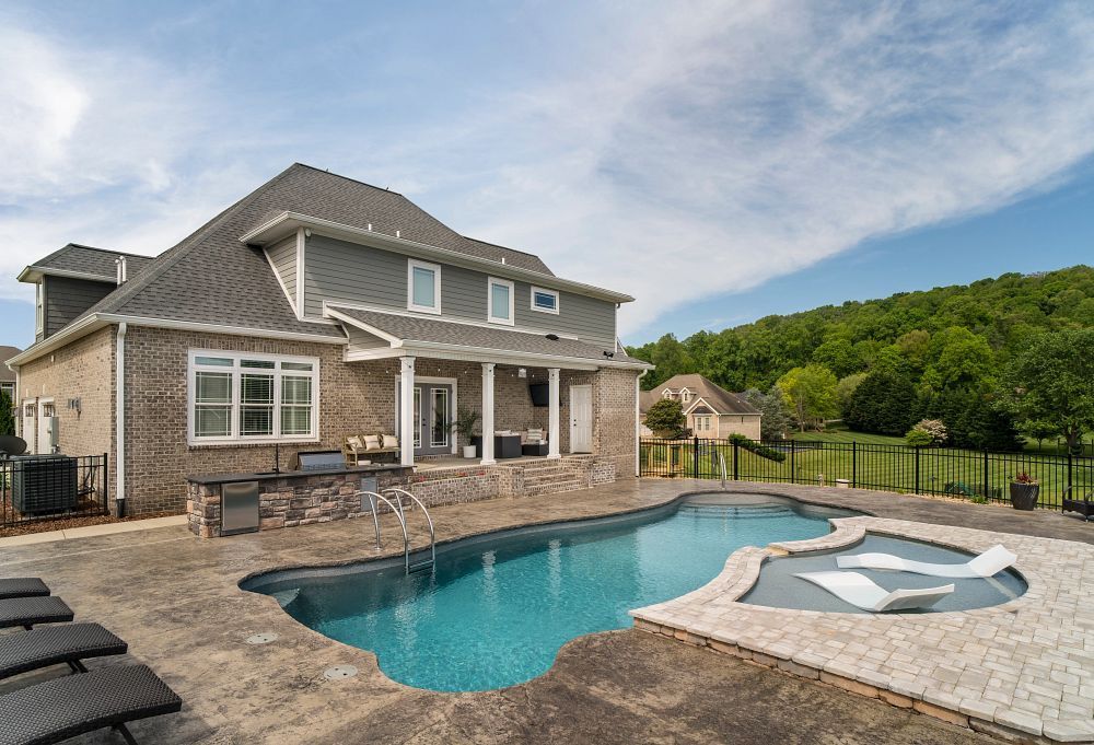 Two-story stone house with a backyard pool and hot tub under a blue sky