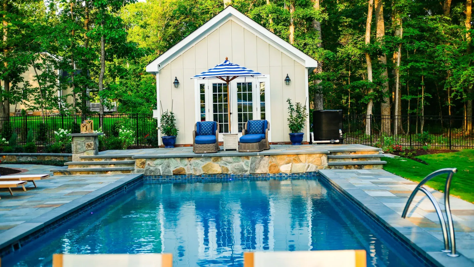 Backyard pool with a small white guest house and patio umbrellas surrounded by trees