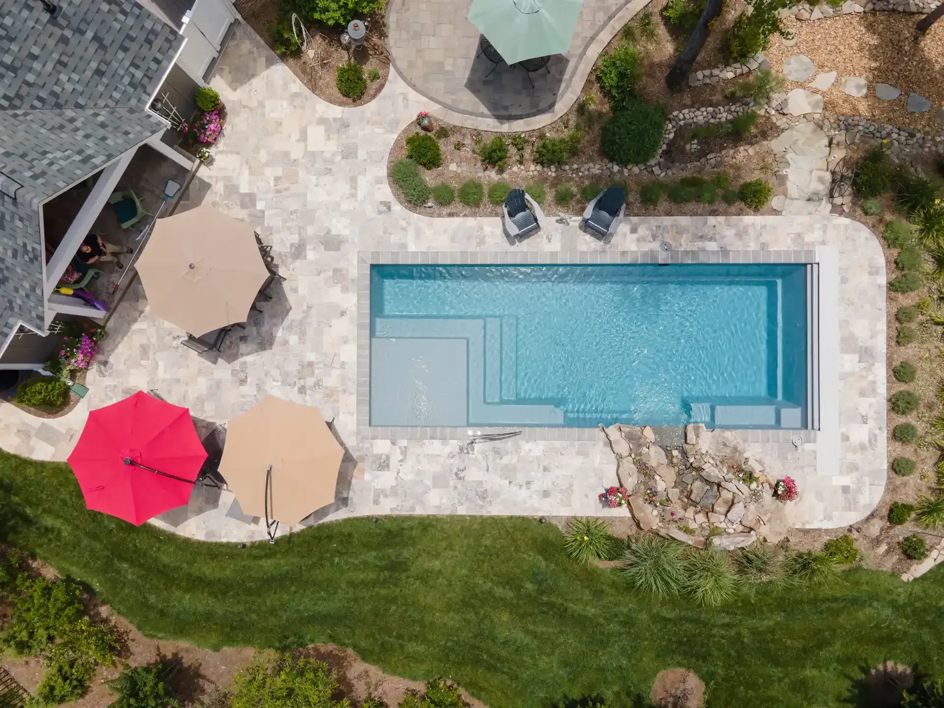 Aerial view of a backyard pool with patio umbrellas, lounge chairs, and landscaped grass.