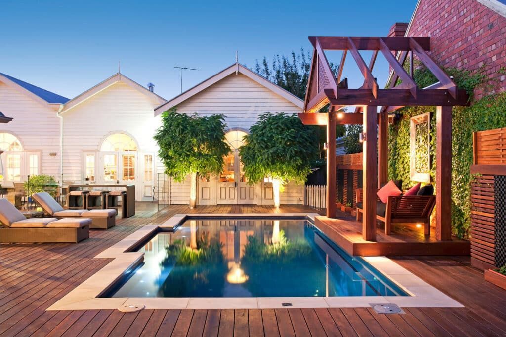 Luxury backyard pool deck with lounge chairs, pergola, and warm evening lighting