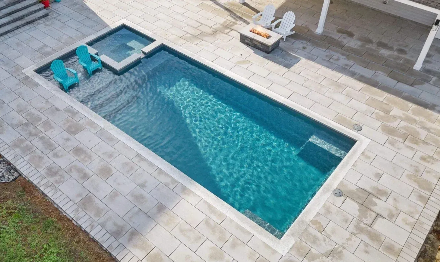 Backyard swimming pool with turquoise water, lounge chairs, and light stone patio tiles