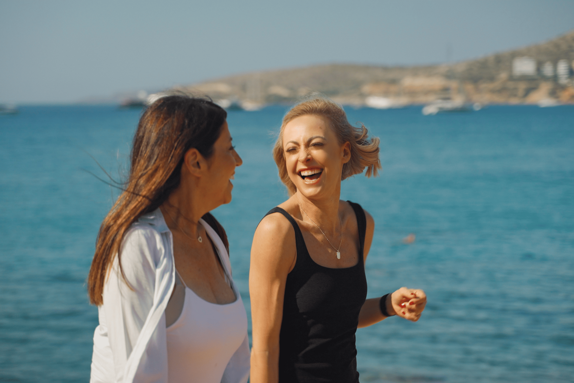 Two people smiling and talking by the ocean on a sunny day