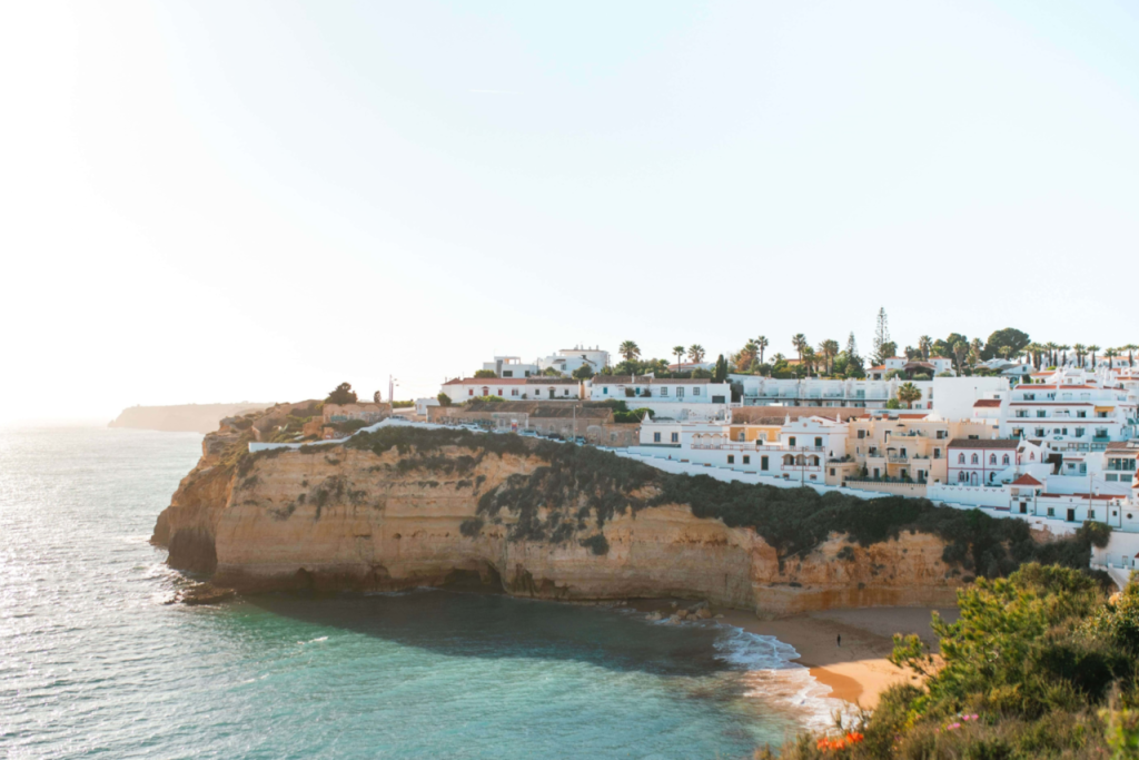 White seaside cliffs lined with white buildings overlooking a turquoise bay at sunset