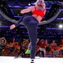 Fitness instructor in red top and black leggings dancing on stage before an audience