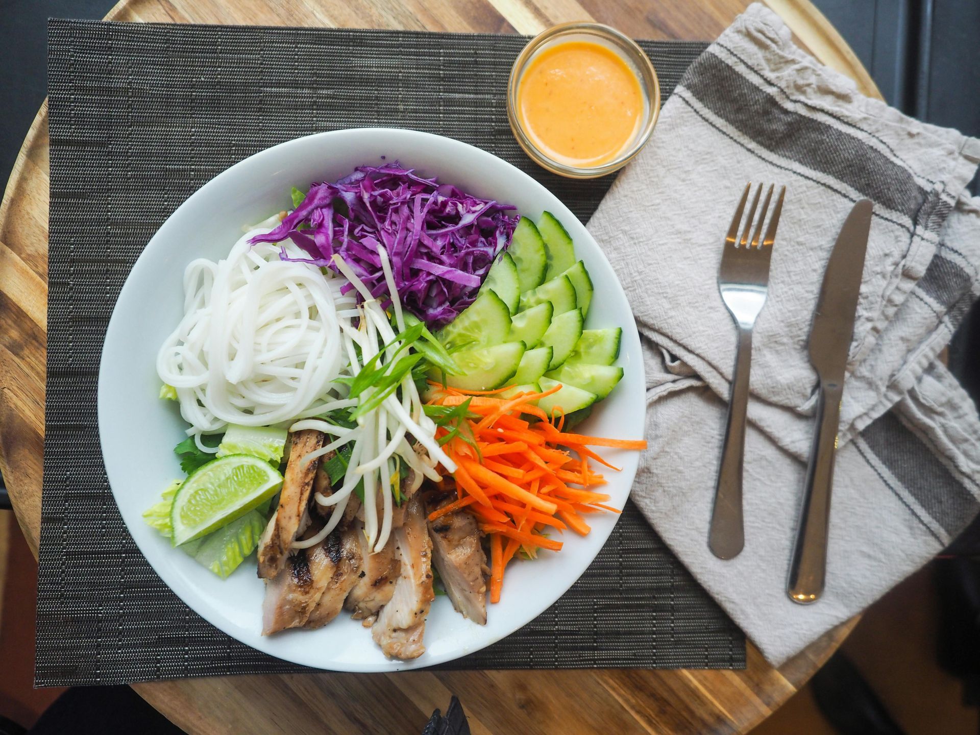 Bowl of colorful noodle salad with chopsticks, sauce cup, and napkin on a placemat