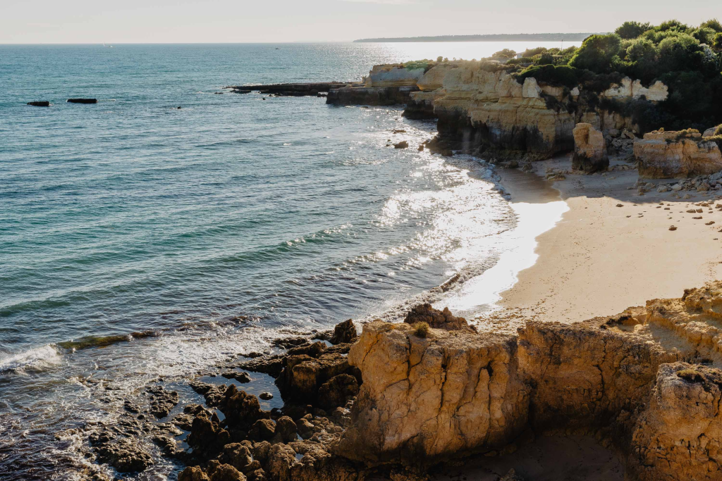 Rocky coastal cove with turquoise water, sandy beach, and bright sunlight on cliffs
