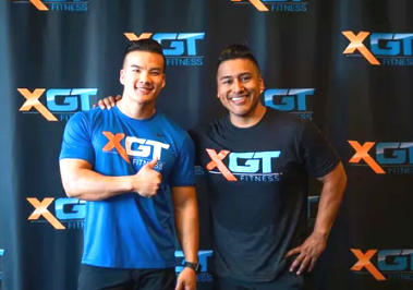 Two men in XGT Fitness shirts smiling and posing in front of an XGT-branded backdrop