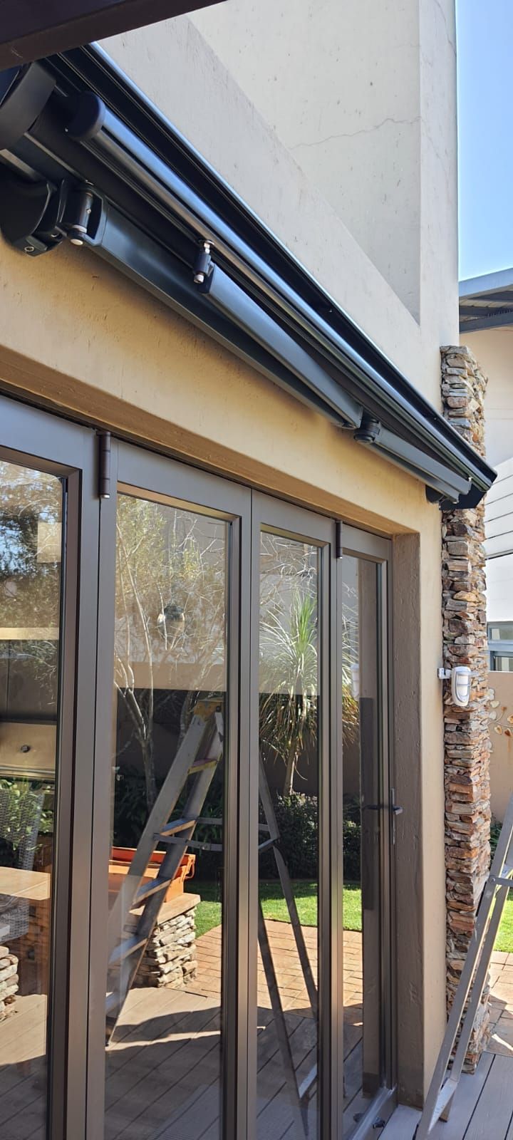 A retractable black awning mounted above glass sliding doors on a tan stucco house exterior.
