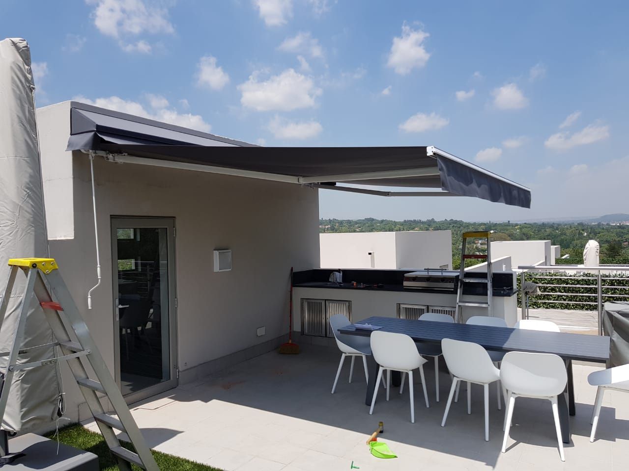 A patio area with a dining table and white chairs under a partially extended dark gray retractable awning.