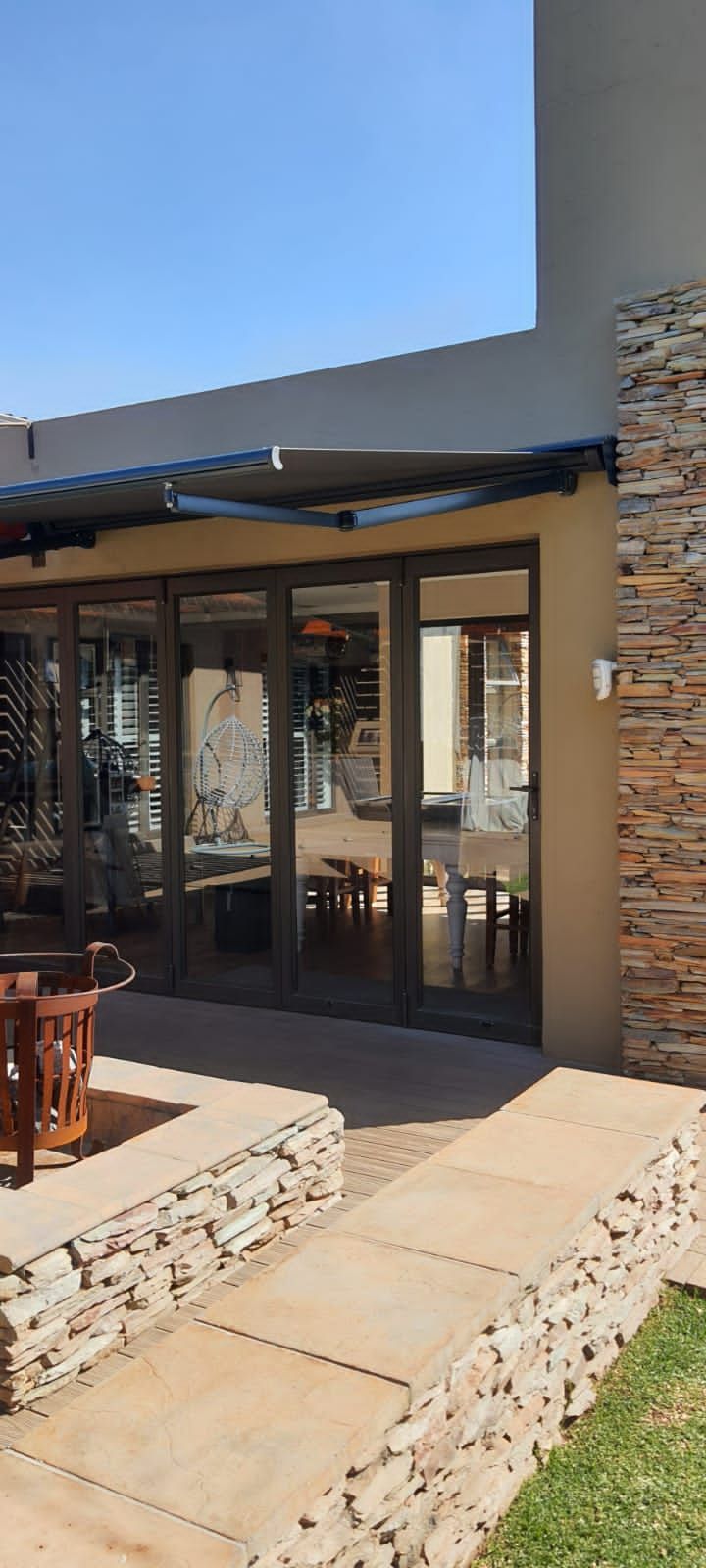 A patio view featuring large glass doors, a stone-clad wall and planter, and a retractable awning under a clear blue sky.