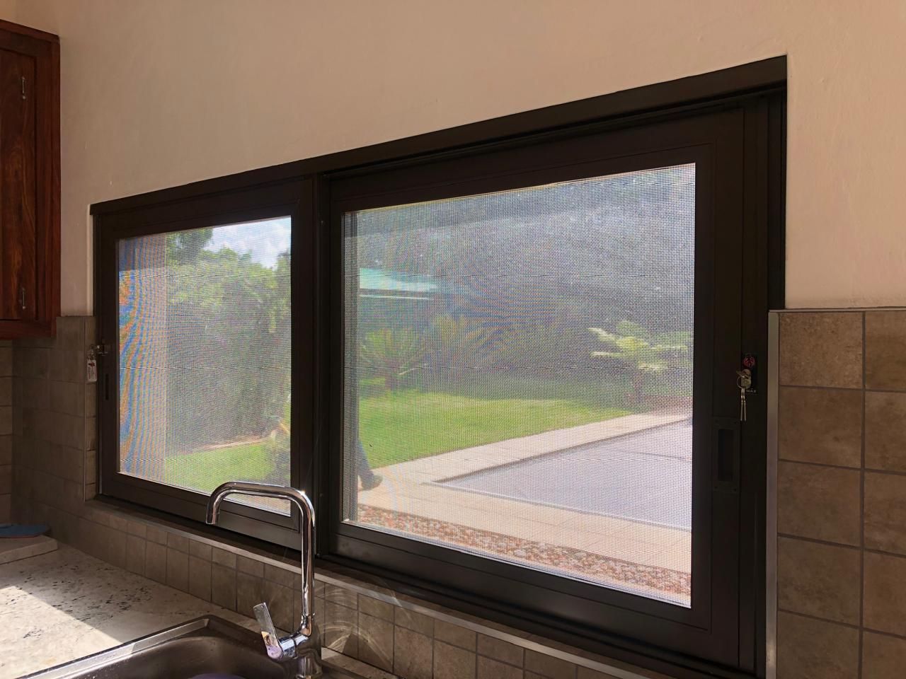 A brown-framed sliding window above a kitchen sink with a security screen installed by SunShade in Pretoria & Johannesburg.