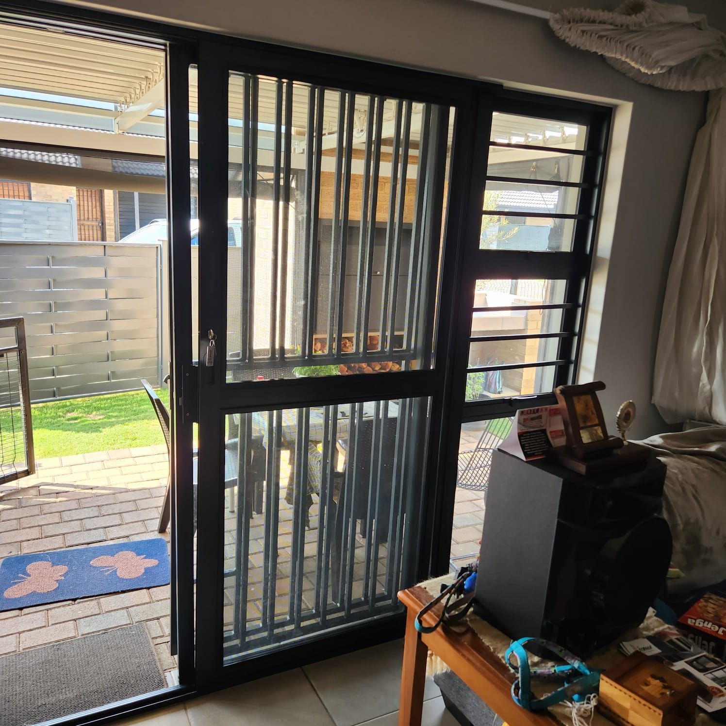 A black metal security gate installed over an open sliding glass door, leading to a brick patio and a yard.