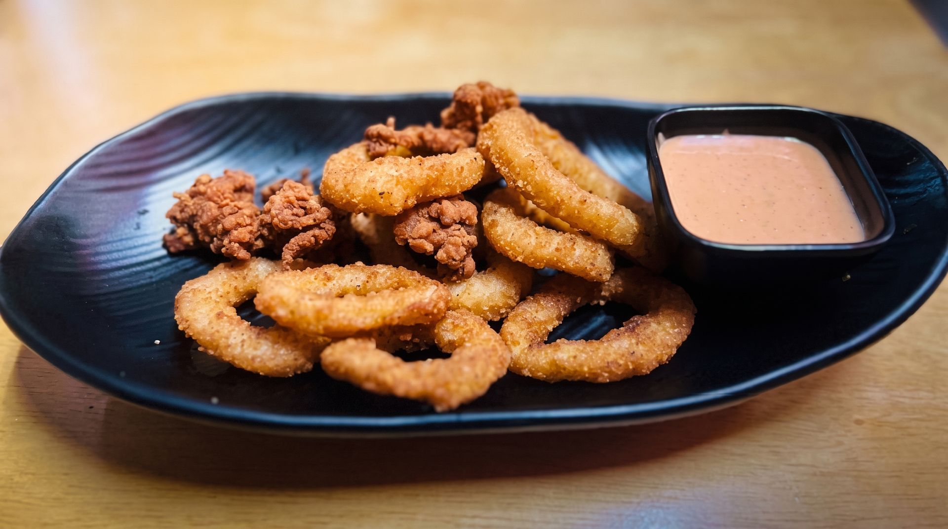 Breaded chicken tenders on a black plate with a side of dipping sauce