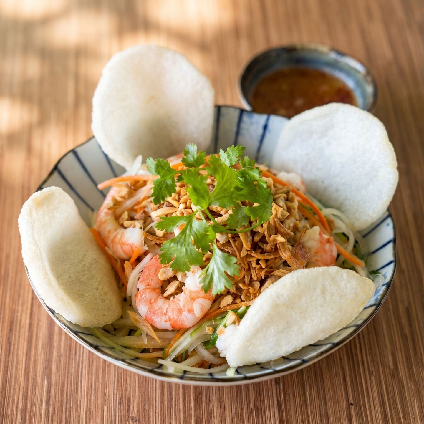 Shrimp salad in a bowl with white rice crackers and fresh herbs on top