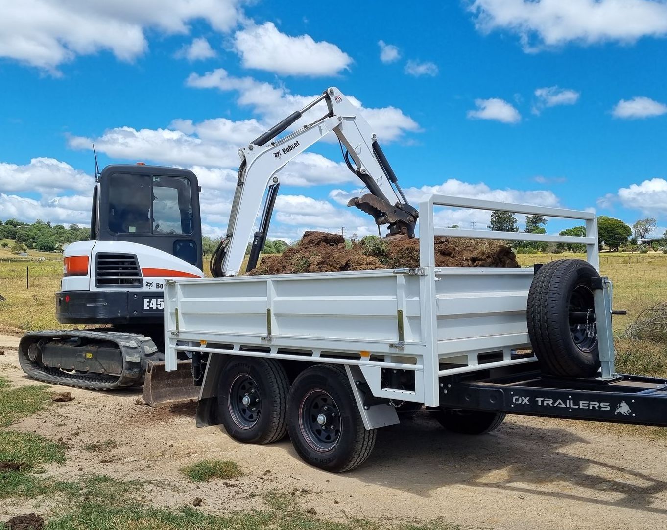 A tipper trailer with extender dropsides and headboard at a farm in Allora QLD being loaded with dirt by an Excavator. 