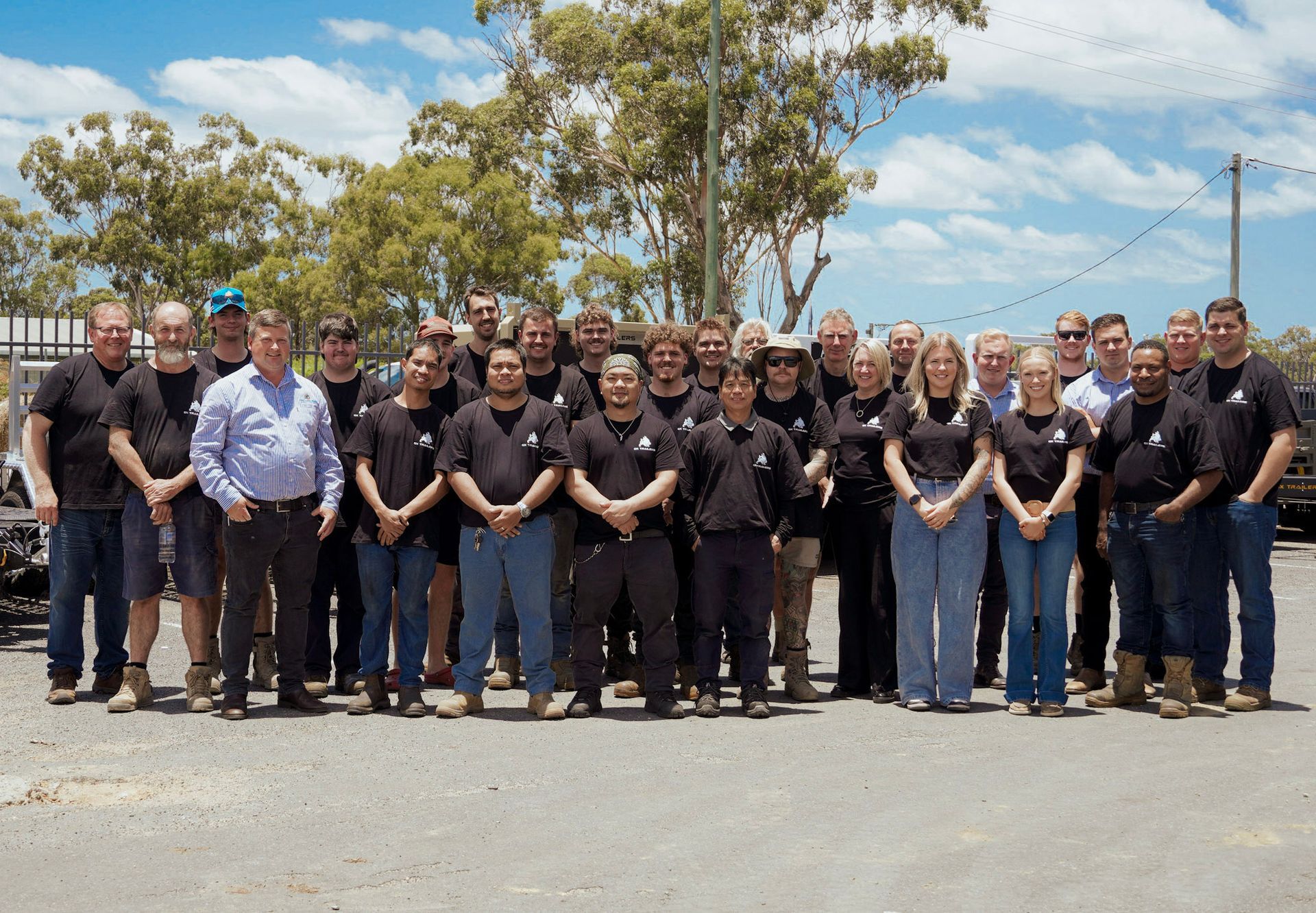 Group photo of the Ox Trailers team in Queensland, showcasing skilled Australian manufacturers and staff in workwear, standing outdoors under a sunny sky.