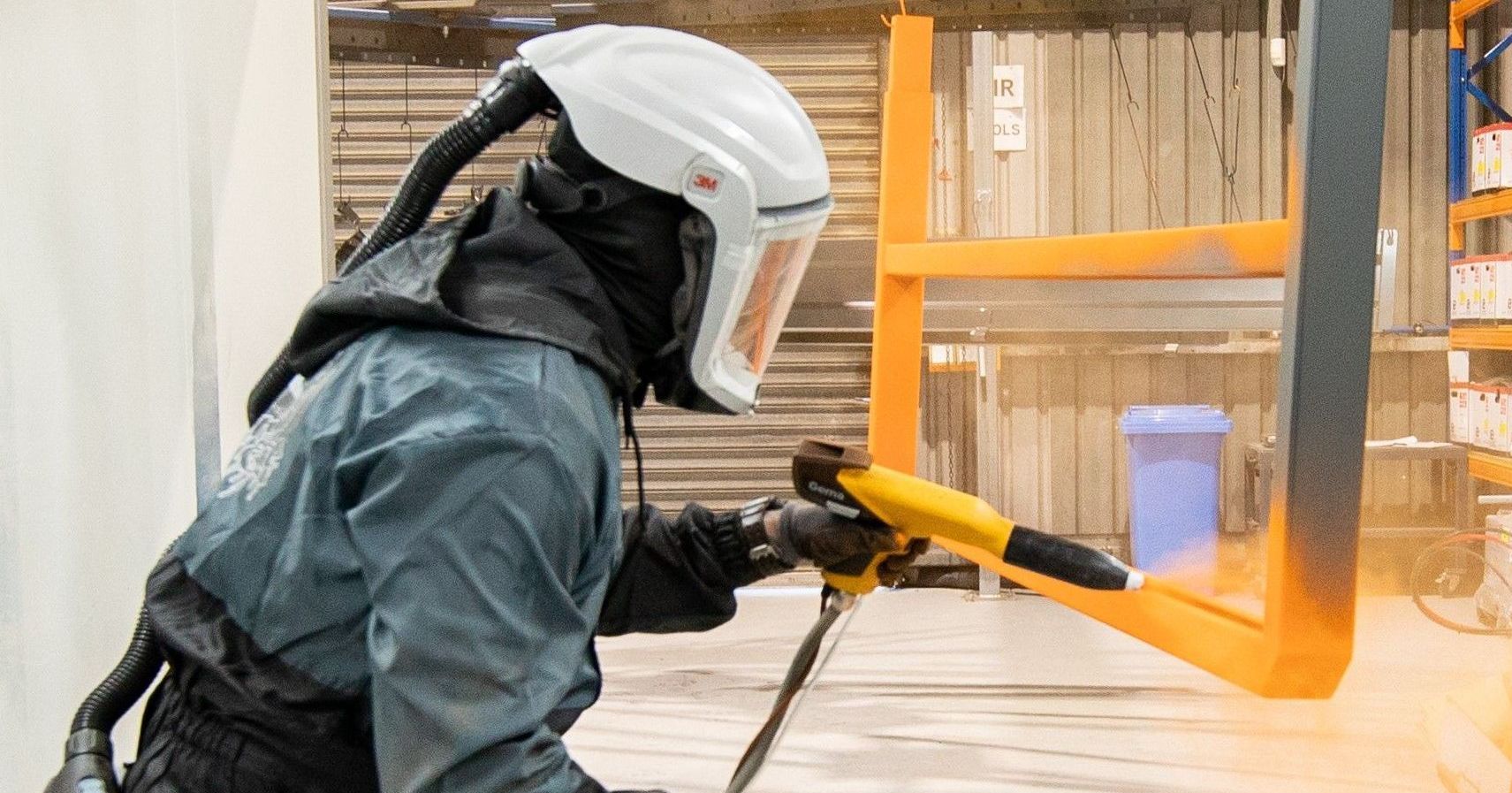 Experienced Powder Coater spraying final topcoat over headboard accessory of trailer.