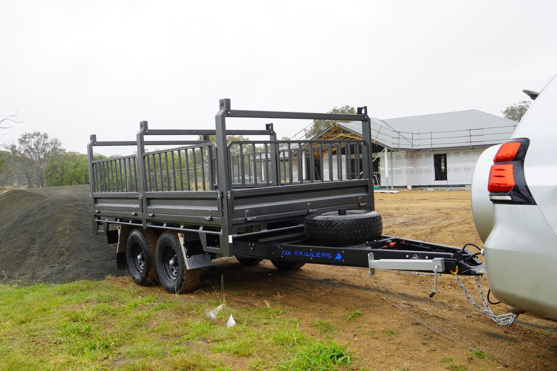Ox Trailers custom 3.5t heavy duty flat deck trailer with ladder racks at a construction site, towed behind a Land Cruiser. 