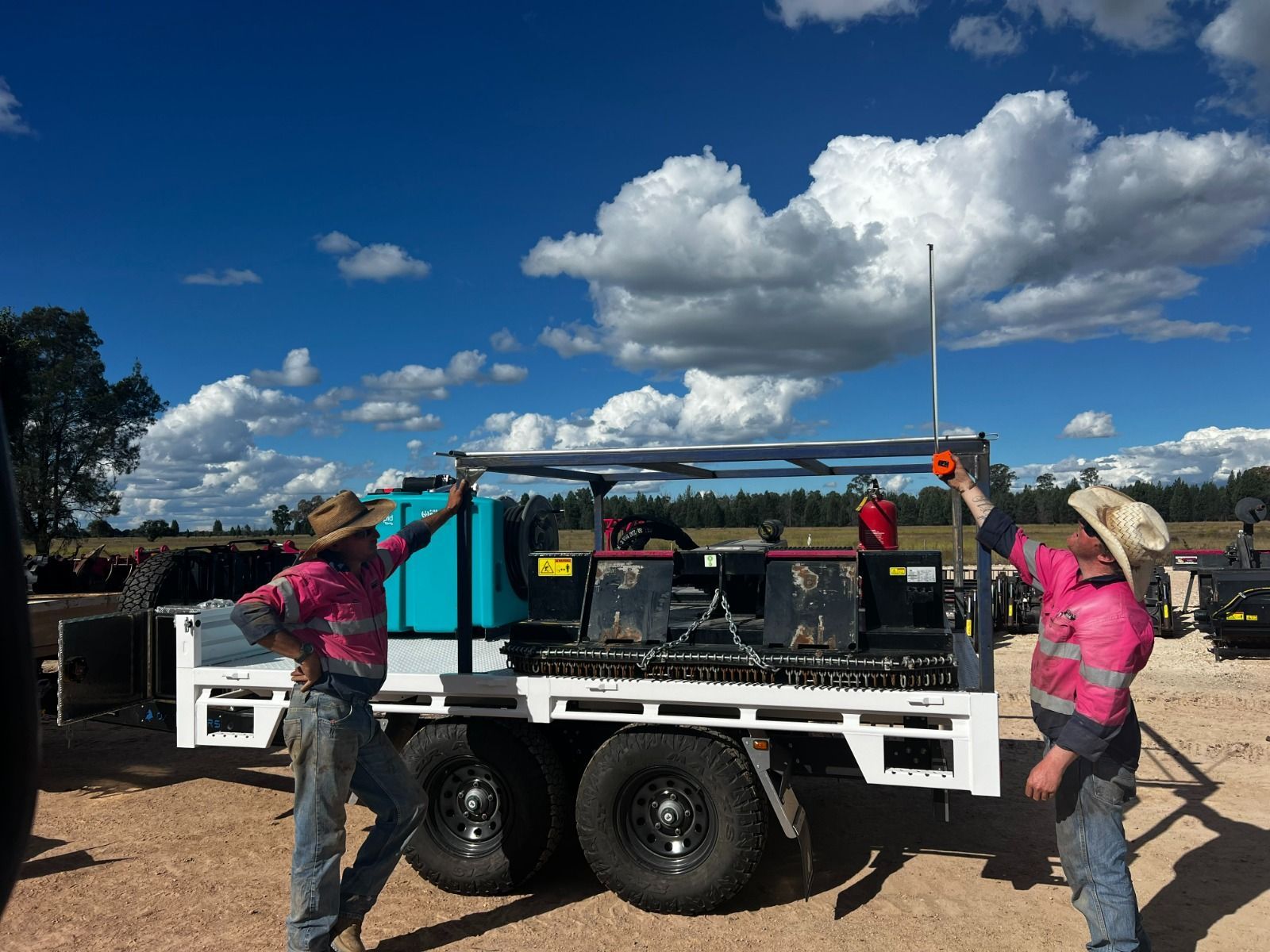 The Monster Hire flat top trailer loaded with machinery while two workers measure how high they can load the trailer. 