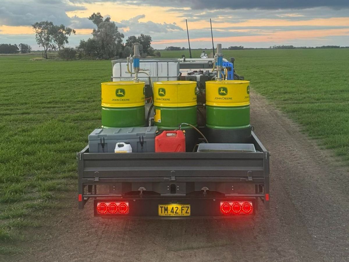 Tom Clarke's Flat Top trailer on a farm road with John Deere barrels, welding machines, and Maxilamp tail lights at dusk.
