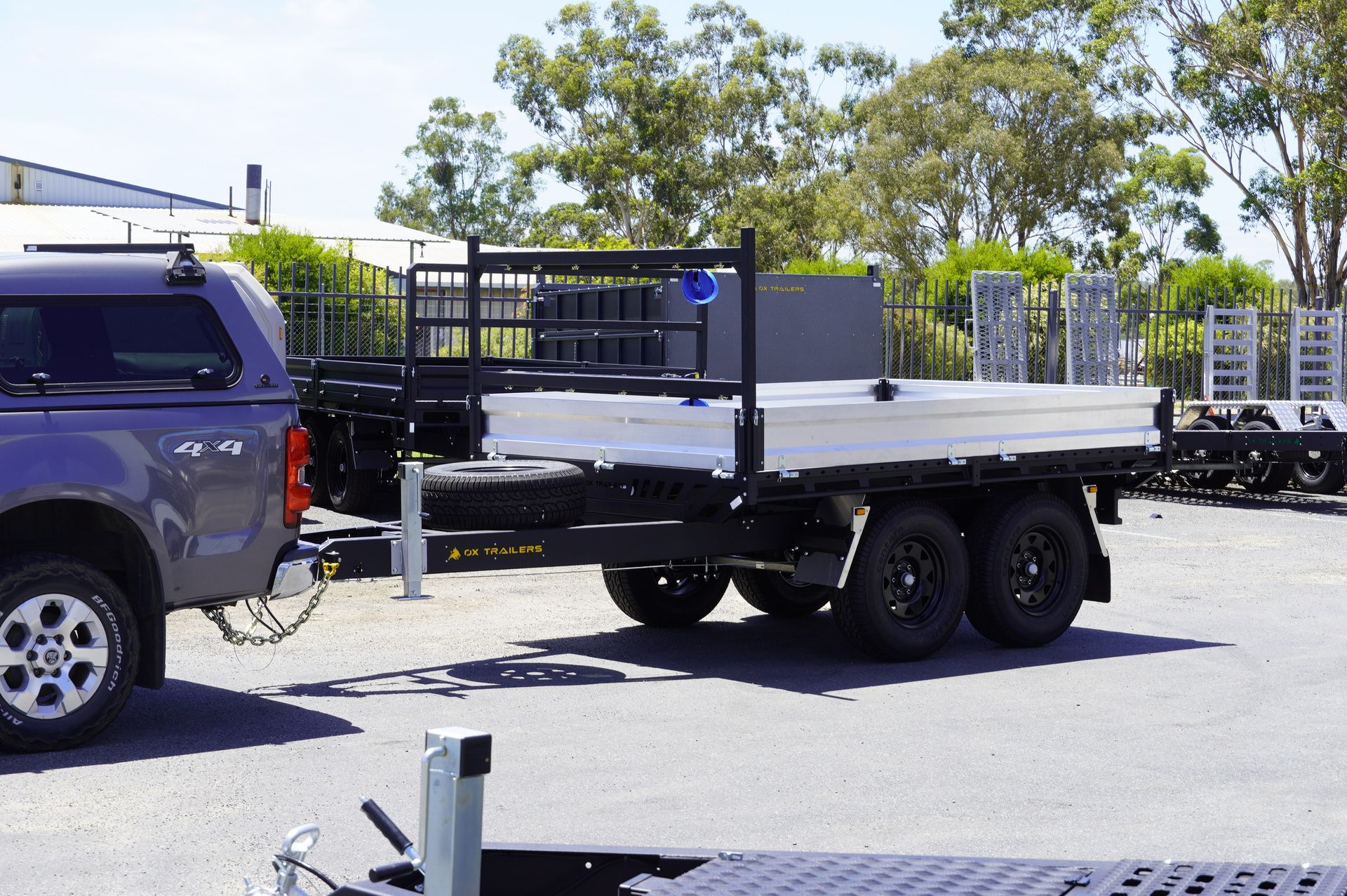heavy duty custom flat top trailer for gee building at rural construction site with toolbox and canopy doors open.