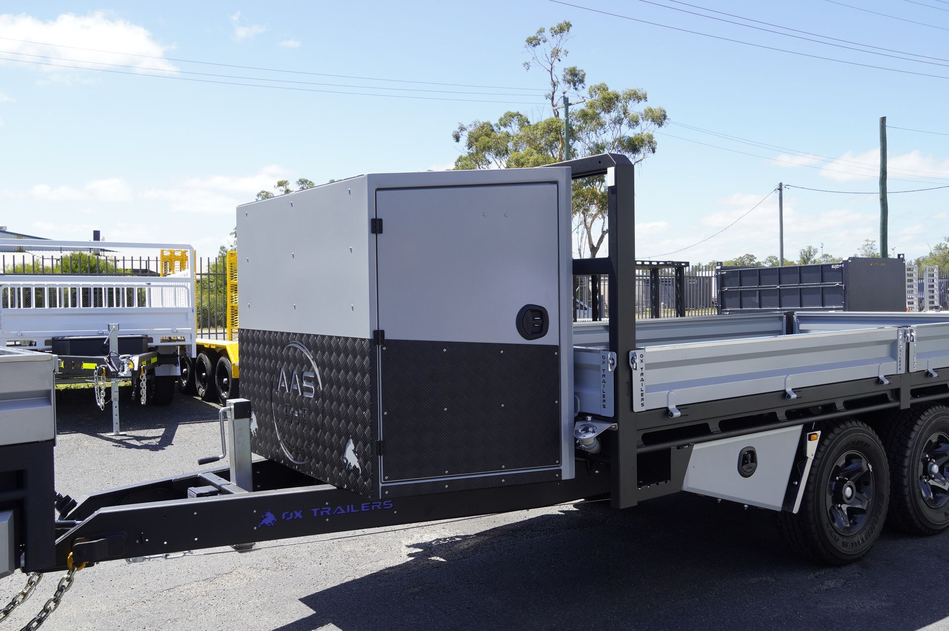heavy duty custom flat top trailer for gee building at rural construction site with toolbox and canopy doors open.
