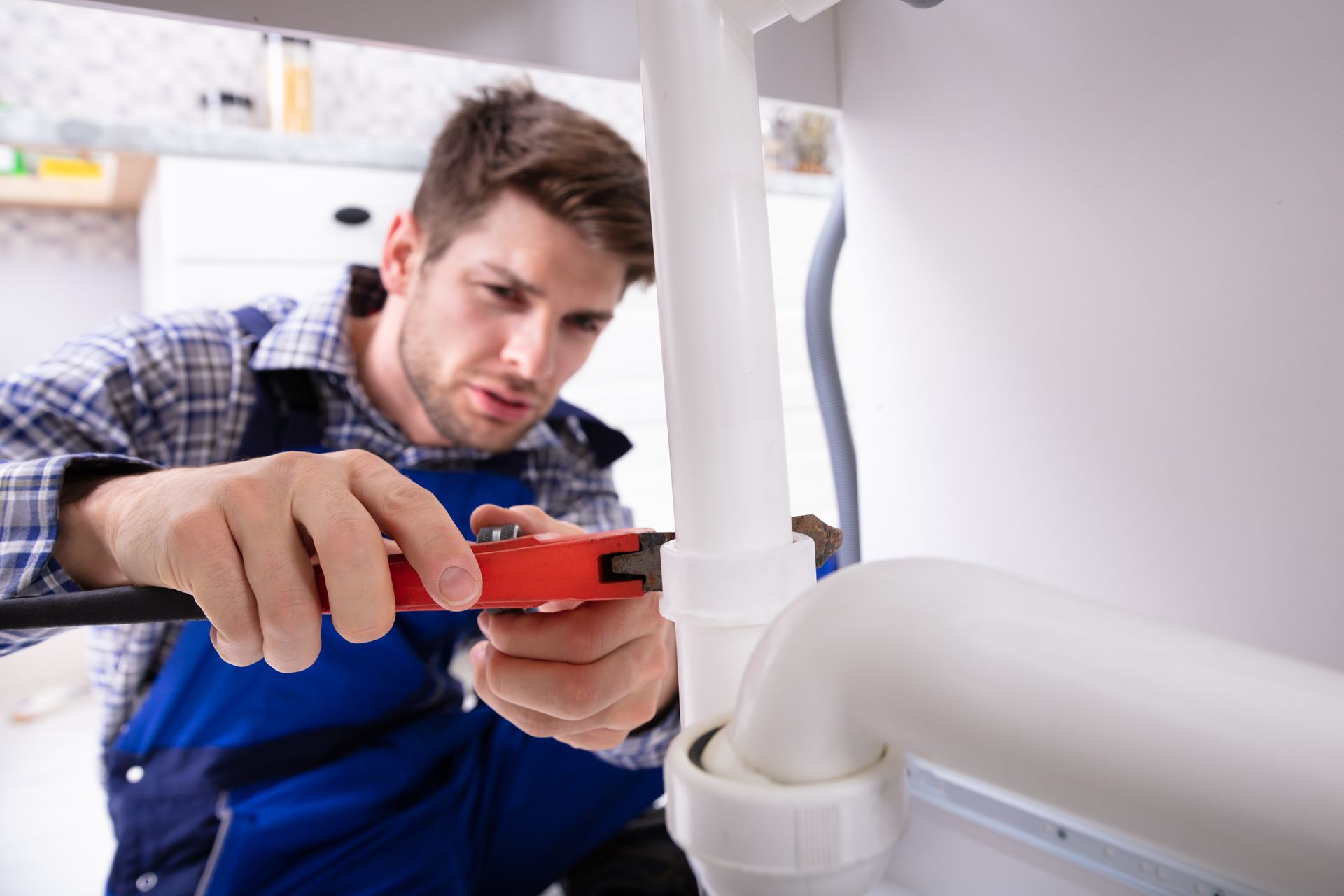 A worker is using a wrench to secure a pipe beneath the sink.
