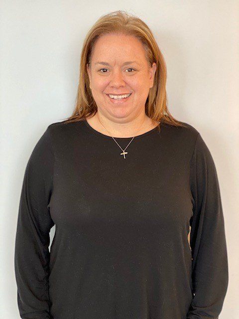 Woman with blonde hair smiling, wearing a black long-sleeved shirt, standing in front of a white wall.