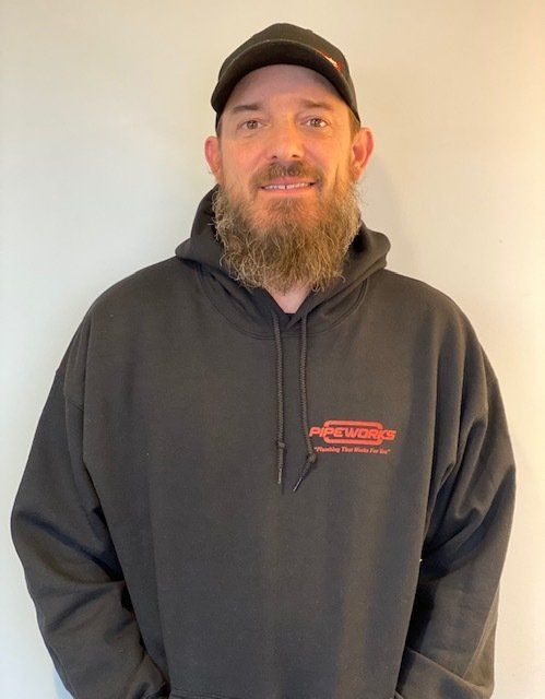Man with a beard, wearing a black hoodie and cap, standing indoors, smiling.