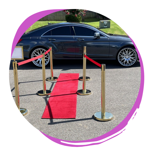 Black sedan on display behind red carpet and stanchions outdoors
