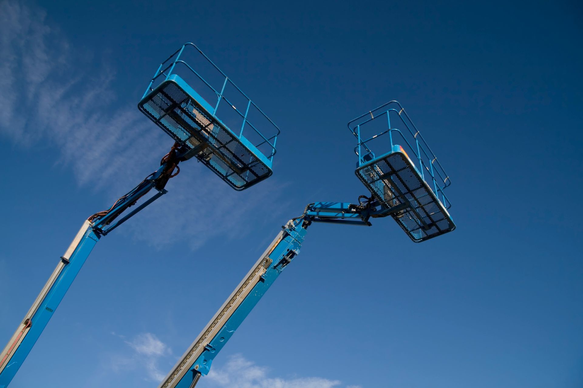 Two blue aerial lifts are against a blue sky.