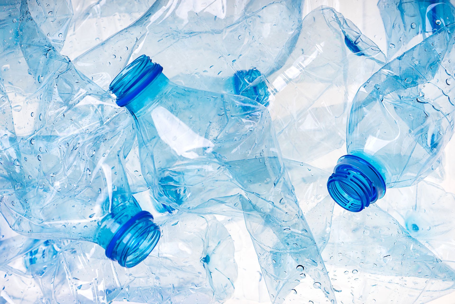 A pile of crushed plastic bottles with blue caps on a white background.
