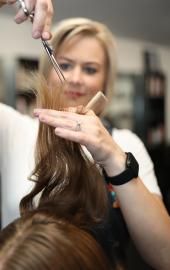 Stylist using scissors to cut a client’s long brown hair in a salon