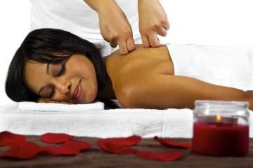 Woman receiving a back massage with red petals and a candle in the foreground