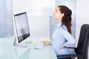 Woman sitting at a desk, leaning back and stretching while facing a computer monitor