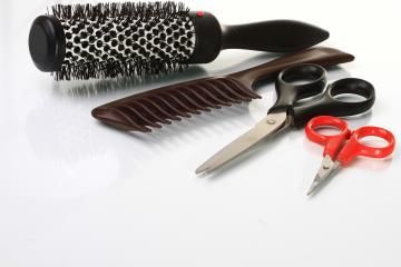 Hair styling tools: round brush, comb, scissors, and red-handled shears on a white surface