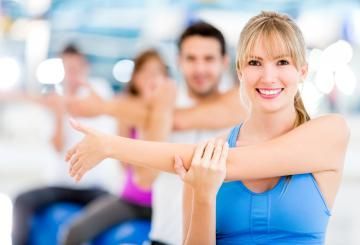 People stretching in a bright fitness class, smiling and extending arms during exercise