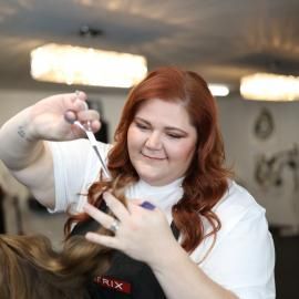 Red-haired stylist cutting a client's hair in a salon, smiling and focused