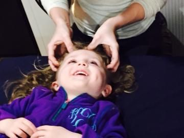 Adult massaging a smiling child’s temples while they lie back in a purple jacket
