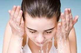 Person washing face with water, eyes closed, against a light background