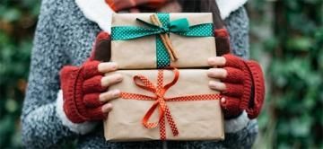 Hands holding two wrapped gifts with teal and red ribbon against a snowy background
