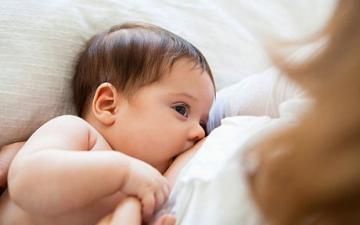 Infant nursing while lying on a white pillow, with a soft blurred background.