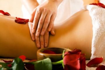 Hands giving a back massage with red rose petals and candles nearby