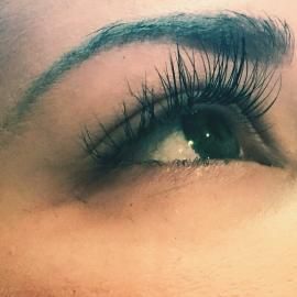 Close-up of a brown eye with long eyelashes and a dark eyebrow, looking upward