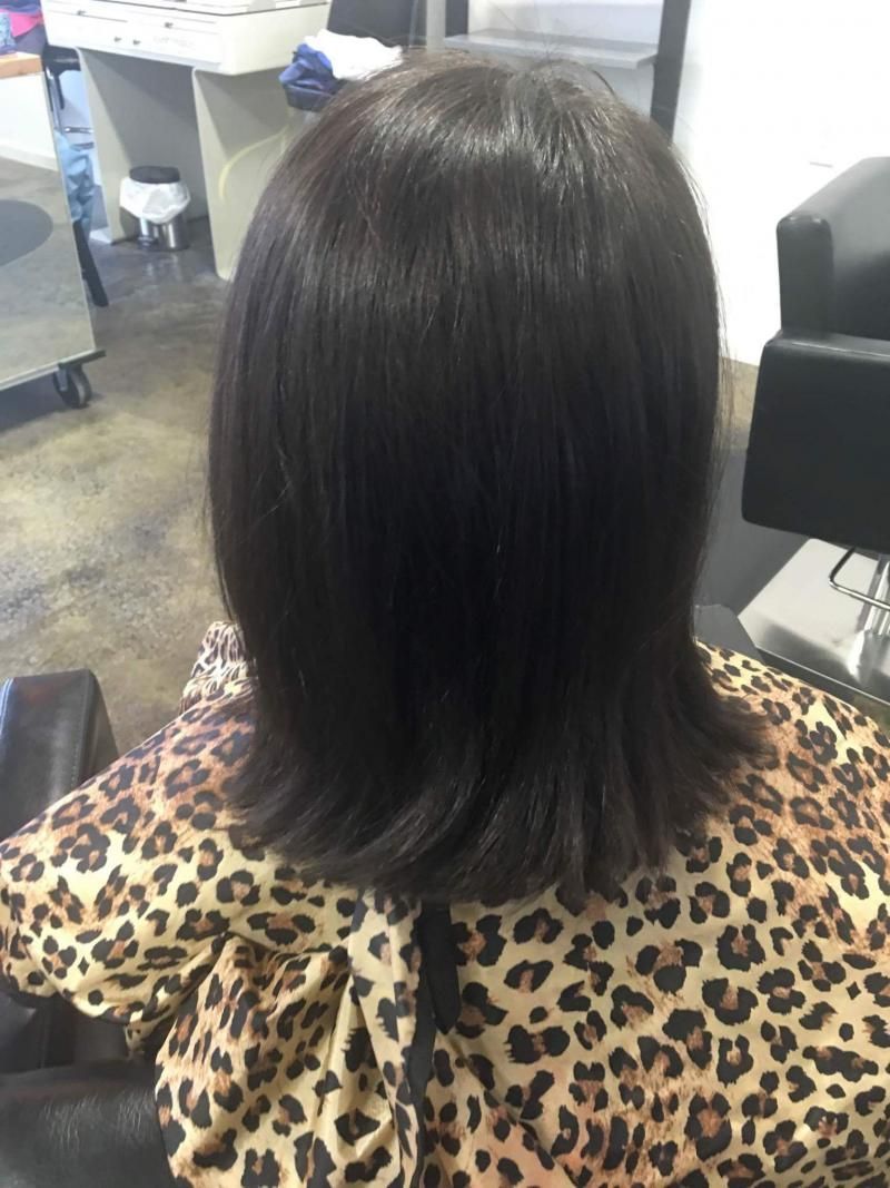 Dark, straight shoulder-length hair viewed from behind in a salon chair, wearing a leopard-print cape.