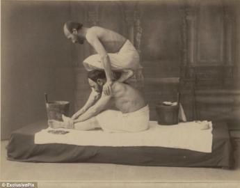 Two stacked performers in white outfits balancing on a platform, with a bucket nearby.