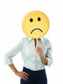 Person in white shirt and navy skirt holding a sad face emoji mask over their head