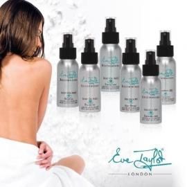 Woman on white background beside six Luv Lap London spray bottles.