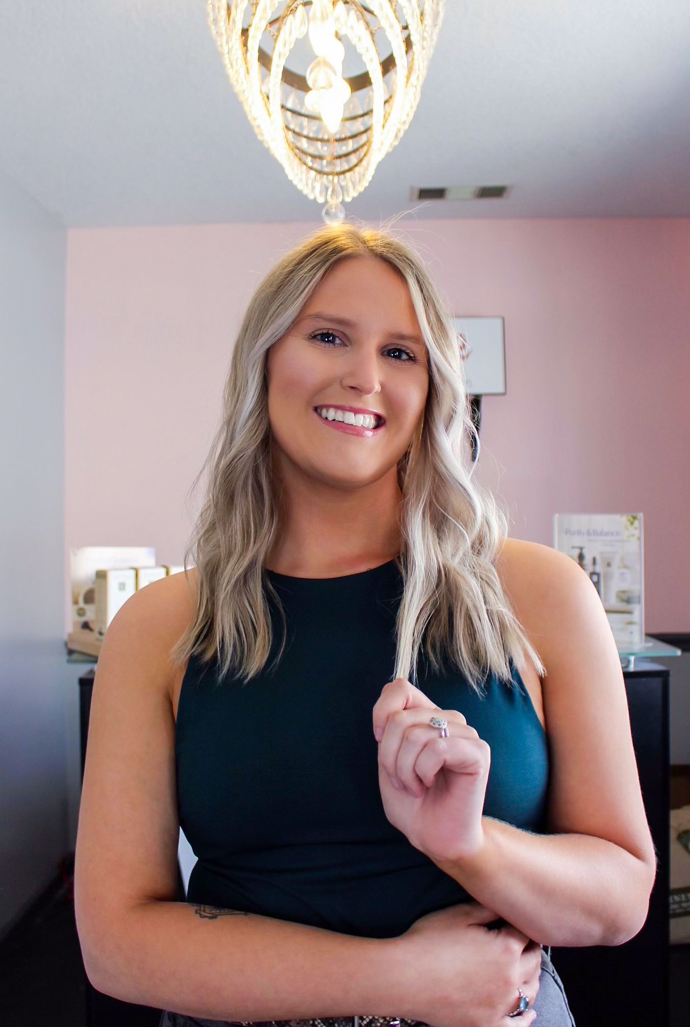 Smiling woman in a black dress standing indoors beneath a gold chandelier
